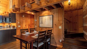 A wooden interior with a dining table set for four, a kitchen area with modern appliances, and a staircase leading to an upper level. - Paradise Found Newly Updated Cabin (Vilas)