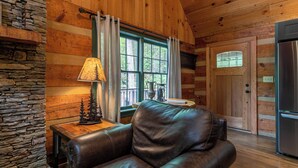 A cozy cabin interior with a leather sofa, a stone wall, a wooden dining table, and a large window with curtains. - Paradise Found Newly Updated Cabin (Vilas)