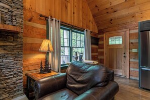 Ein gemütliches Blockhaus-Interieur mit Ledersofa, Steinwand, Holztisch und großem Fenster mit Vorhängen.