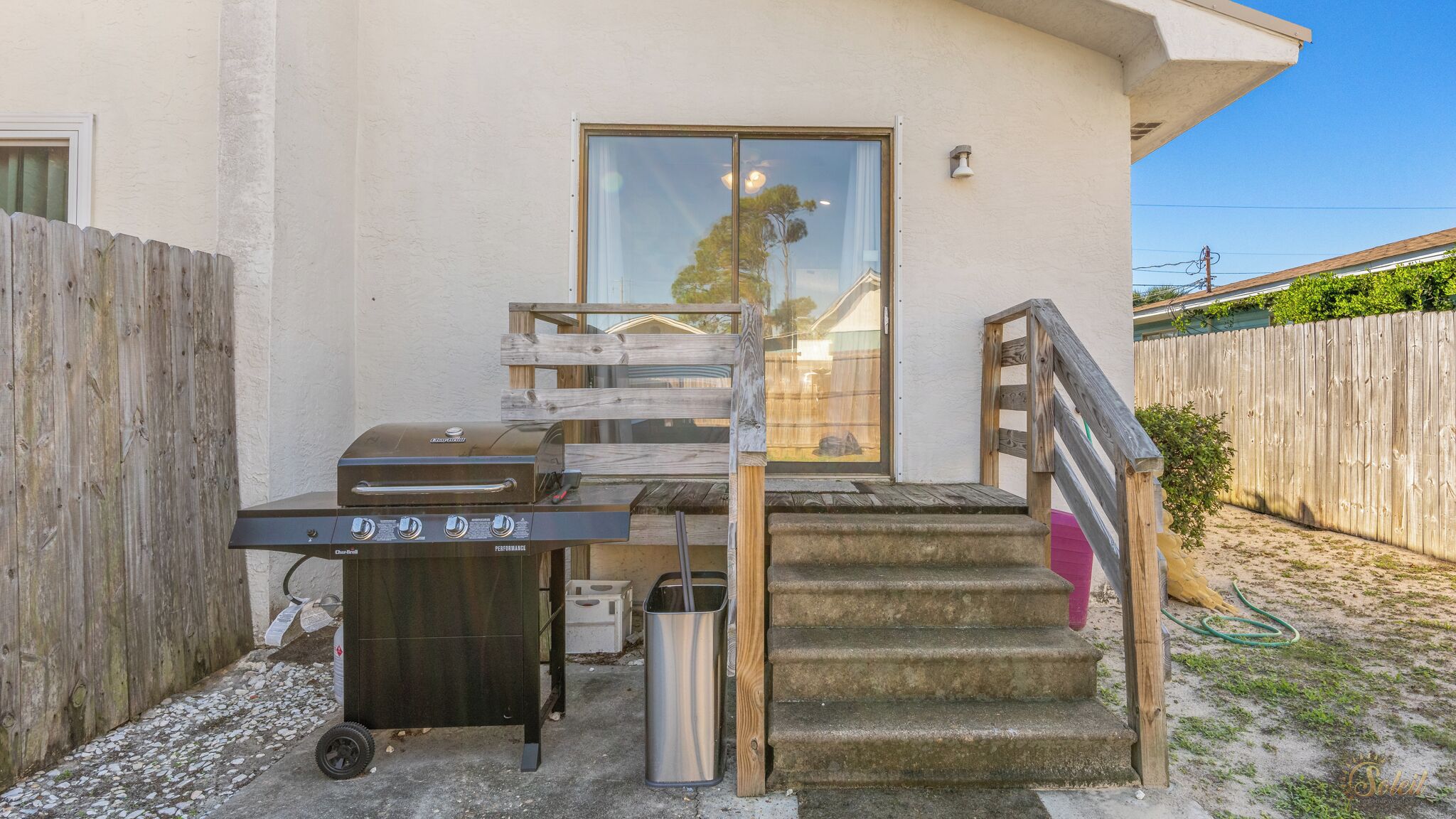 A barbecue grill, a trash can, and a wooden staircase leading to a house.
