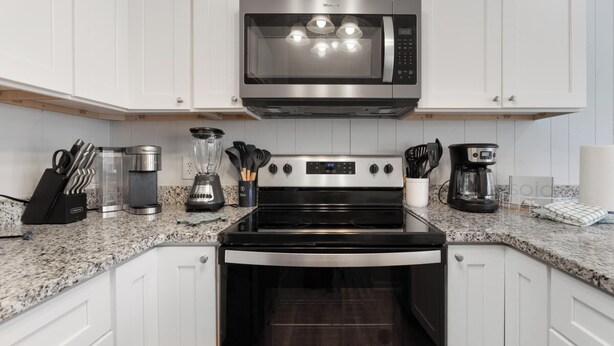 A modern kitchen with white cabinets, a stainless steel microwave, a black stove, a coffee maker, and a blender.