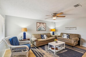 Ein Wohnzimmer mit Deckenventilator, zwei Sofas, einem Couchtisch und einem Korbstuhl.