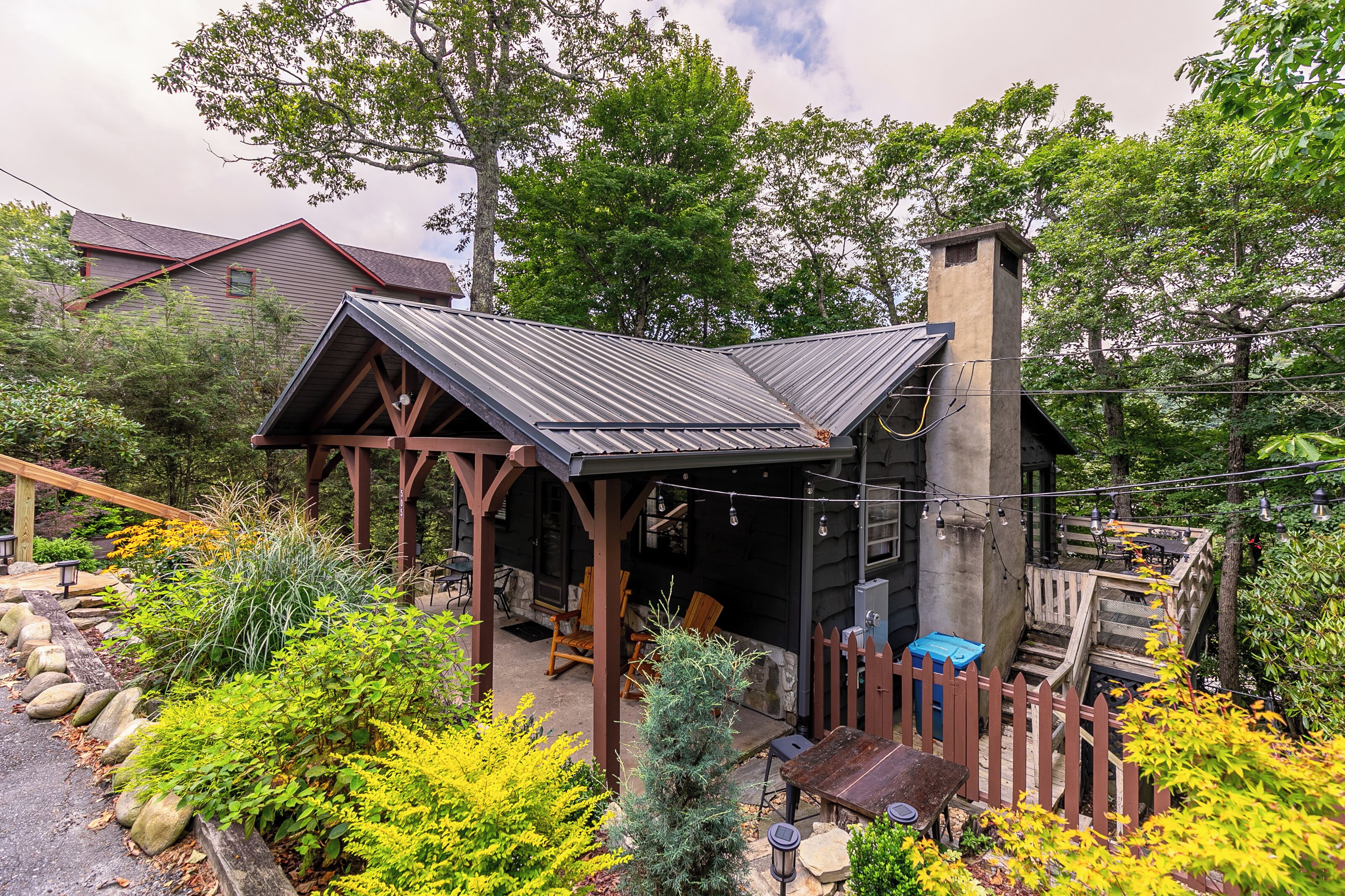 A rustic cabin with a metal roof, wooden deck, and a stone chimney.