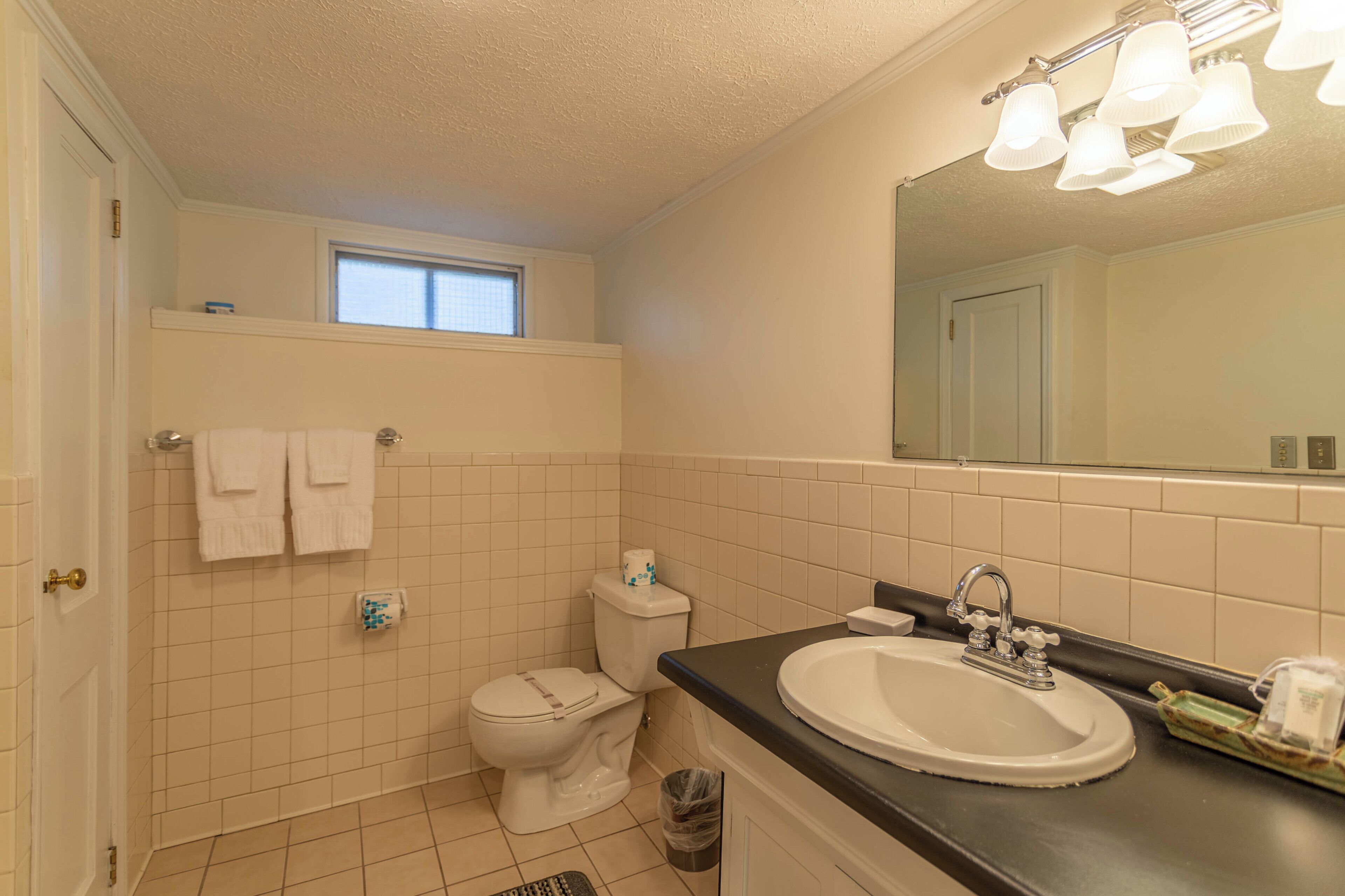 A bathroom with a toilet, sink, and a window above the toilet.