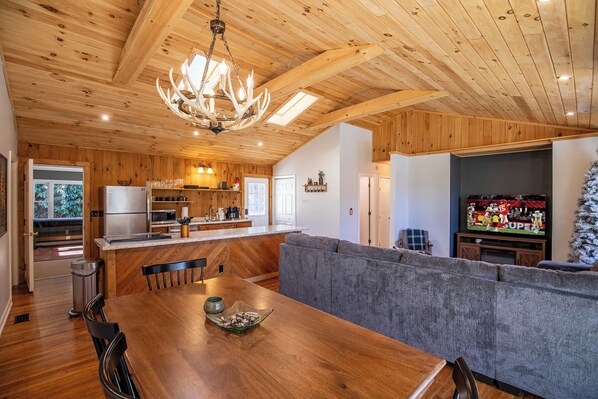 Ein Holzinterieur mit Esstisch, Sofa, Küchenbereich und Fernseher.