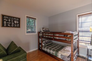 A bunk bed room with a framed animal print on the wall, a window with blinds, and a green couch. - Snaggys Retreat (Boone)