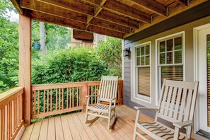 A wooden deck with two rocking chairs, a covered porch, and a view of a house with a window and blinds. - Peace at Echota (Boone)