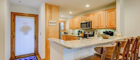 Una cocina con armarios de madera, microondas, estufa y una barra desayunadora con sillas de madera.