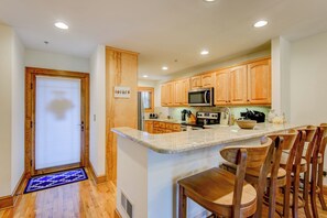 A kitchen with wooden cabinets, a microwave, a stove, and a breakfast bar with wooden chairs. - Peace at Echota (Boone)