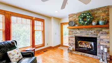 A spacious living room with a fireplace, wooden flooring, and large windows.