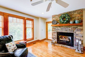 Amplia sala de estar con chimenea, piso de madera y ventanas grandes.