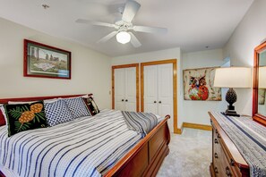 Une chambre à coucher avec un lit, un ventilateur de plafond, une commode et une porte.