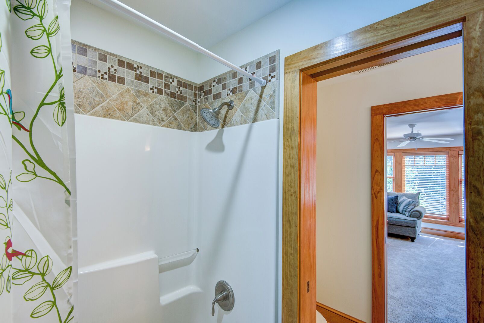 A bathroom with a shower, tiled walls, and a door leading to a living room.