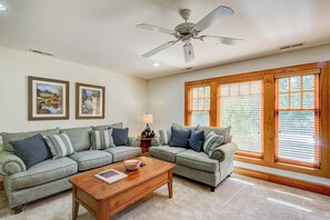 A living room with two grey sofas, a wooden coffee table, and a ceiling fan. There are two framed pictures on the wall and a window with blinds. - Peace at Echota (Boone)