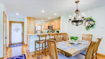 A modern kitchen with wooden cabinets, a central island, and a dining area with a chandelier and floral decoration.