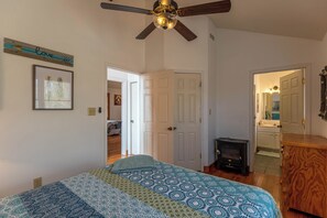 Un dormitorio con cama, ventilador de techo, cómoda de madera y una puerta que da a otra habitación.