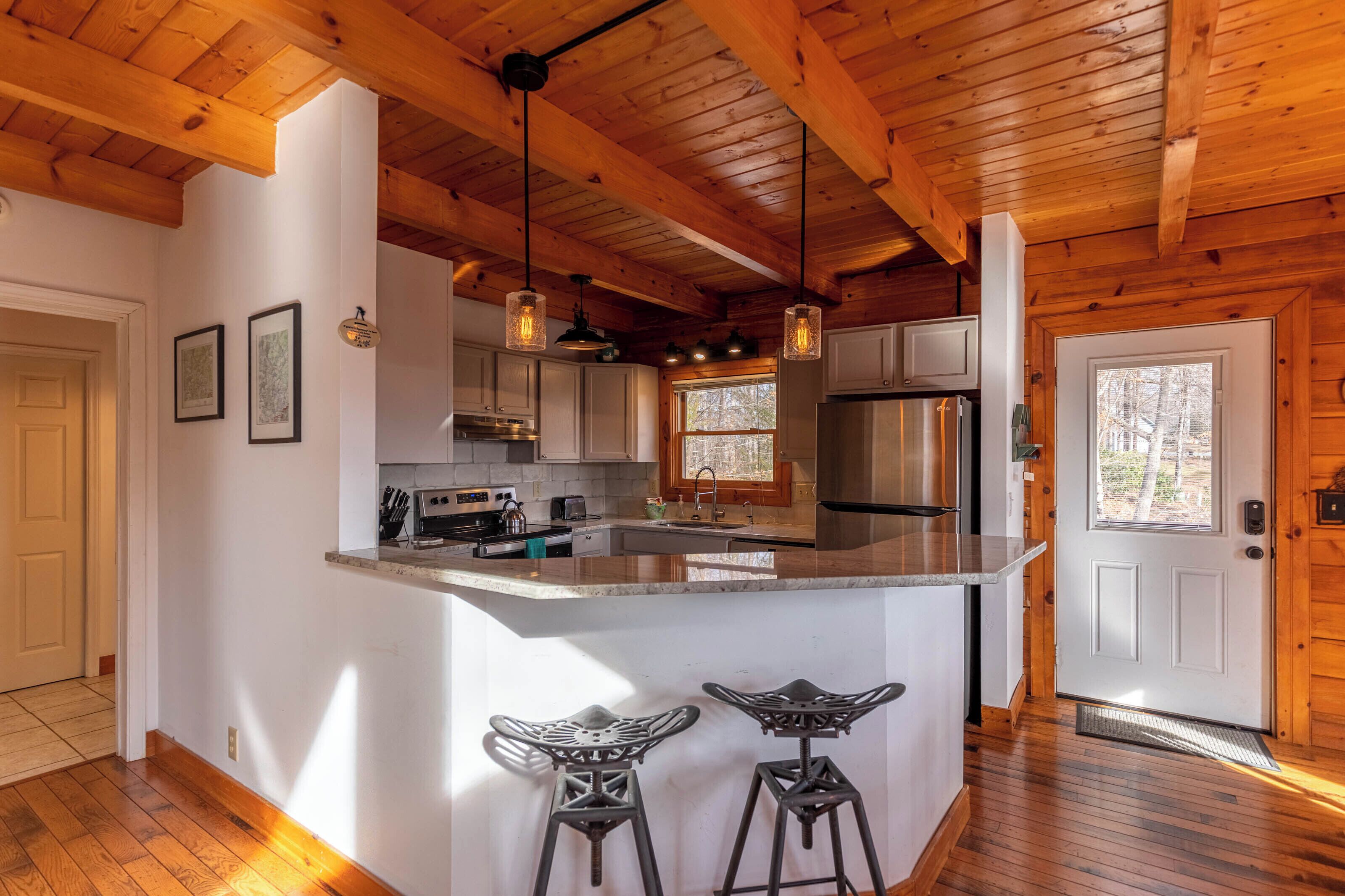 A kitchen with wooden beams, a central island with stools, and a refrigerator.