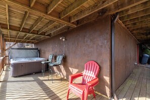 Una terraza de madera con un jacuzzi, dos sillas y una silla Adirondack roja.