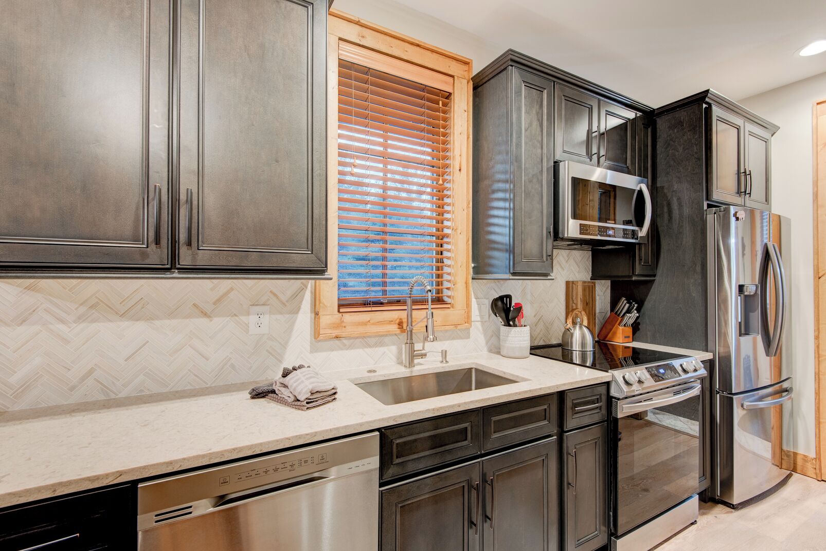 A modern kitchen with dark cabinets, a stainless steel refrigerator, a microwave, and a dishwasher.
