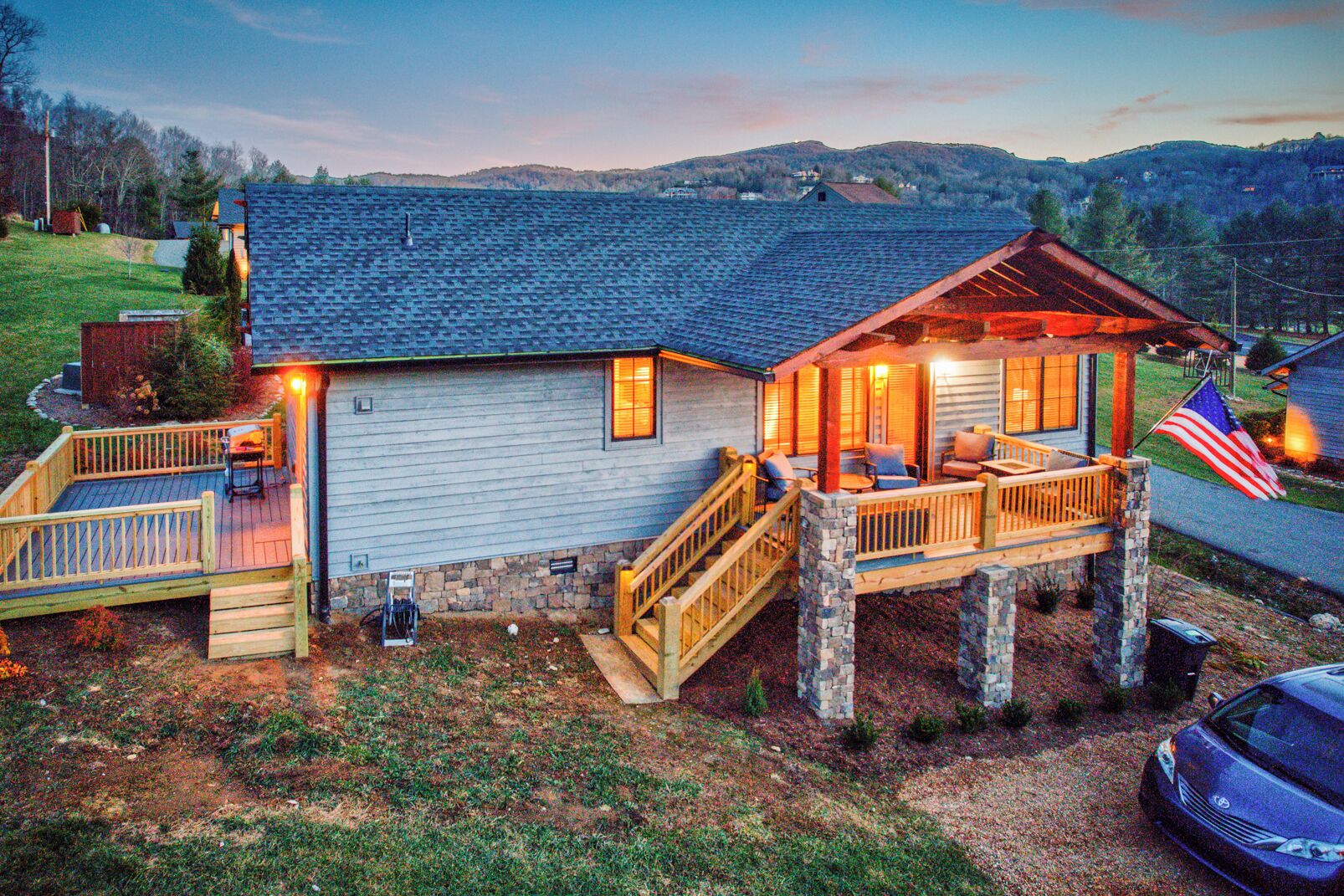 A two-story cabin with a deck and outdoor seating area, surrounded by a wooded landscape.