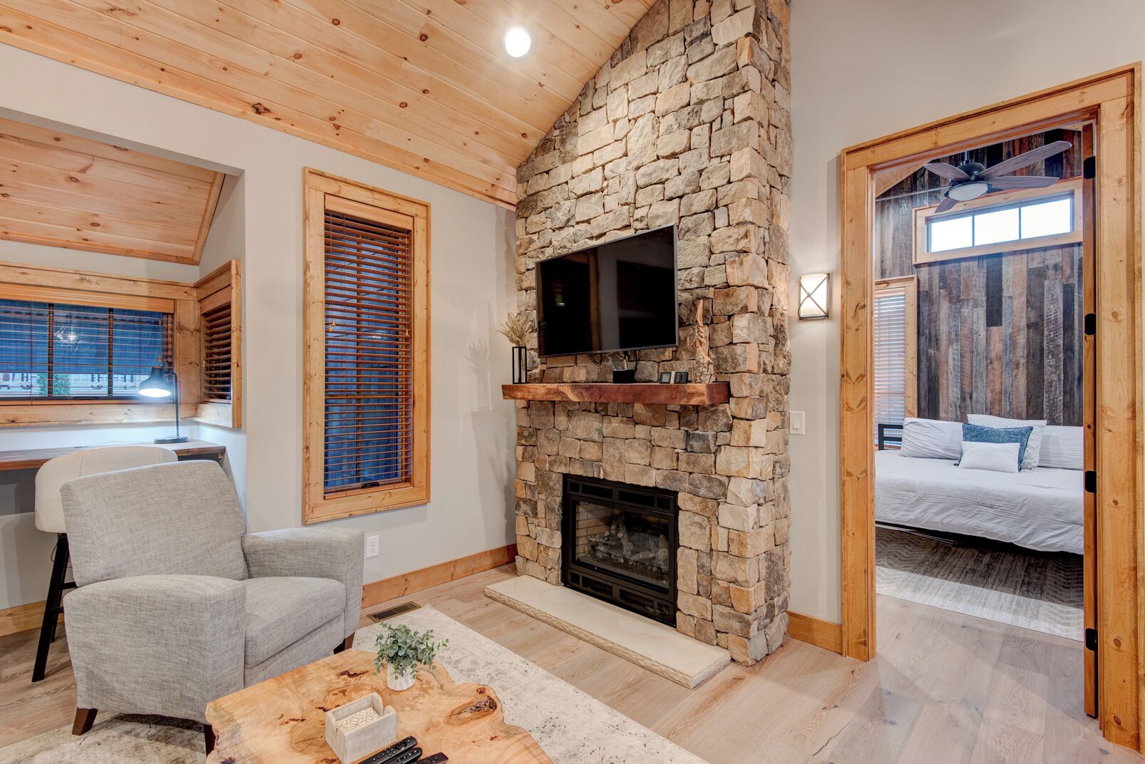 A cozy living room with a stone fireplace, a comfortable gray armchair, and a wooden coffee table.