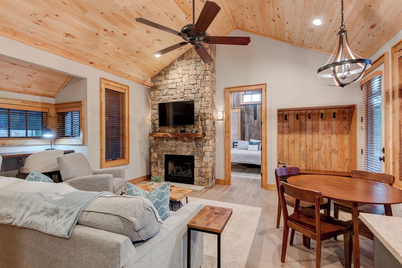 A cozy living room with a stone fireplace, a ceiling fan, and a dining area with wooden furniture.