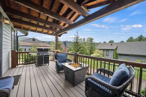 A covered deck with wicker furniture, a grill, and a fire pit. - River Rock (Banner Elk)