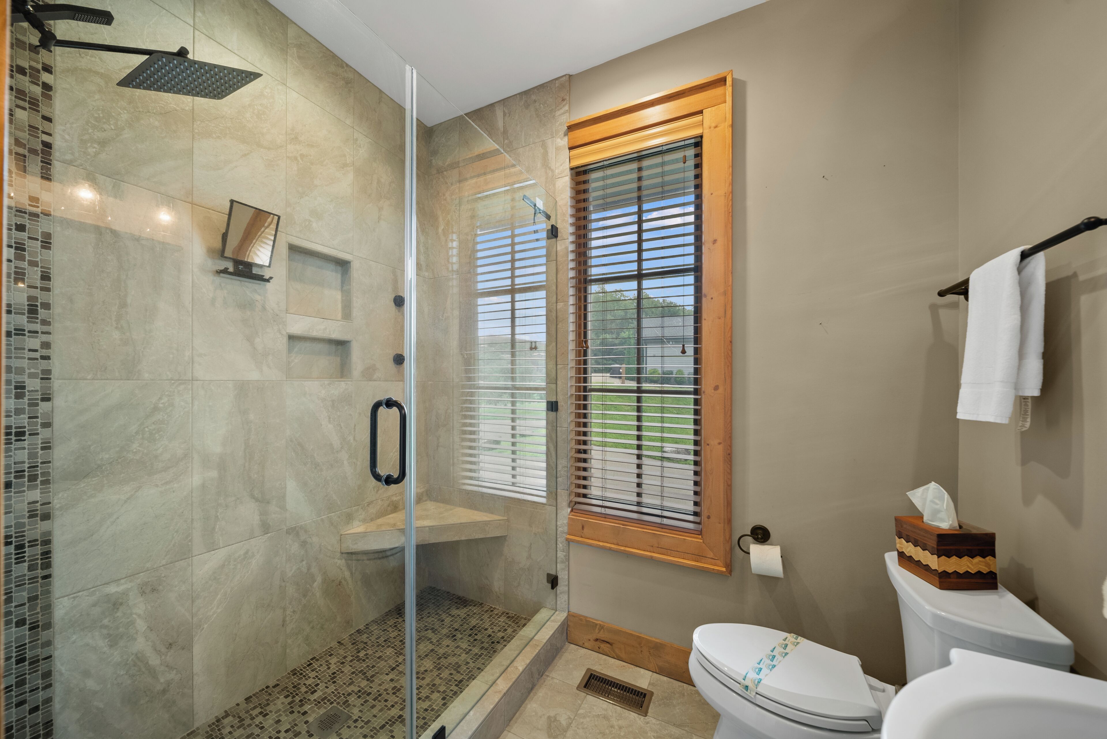 A modern bathroom with a glass-enclosed shower, a toilet, and a window with blinds.