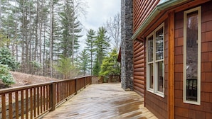 A wooden deck with a stone wall and windows, surrounded by a forest. - The Forge (Lansing)