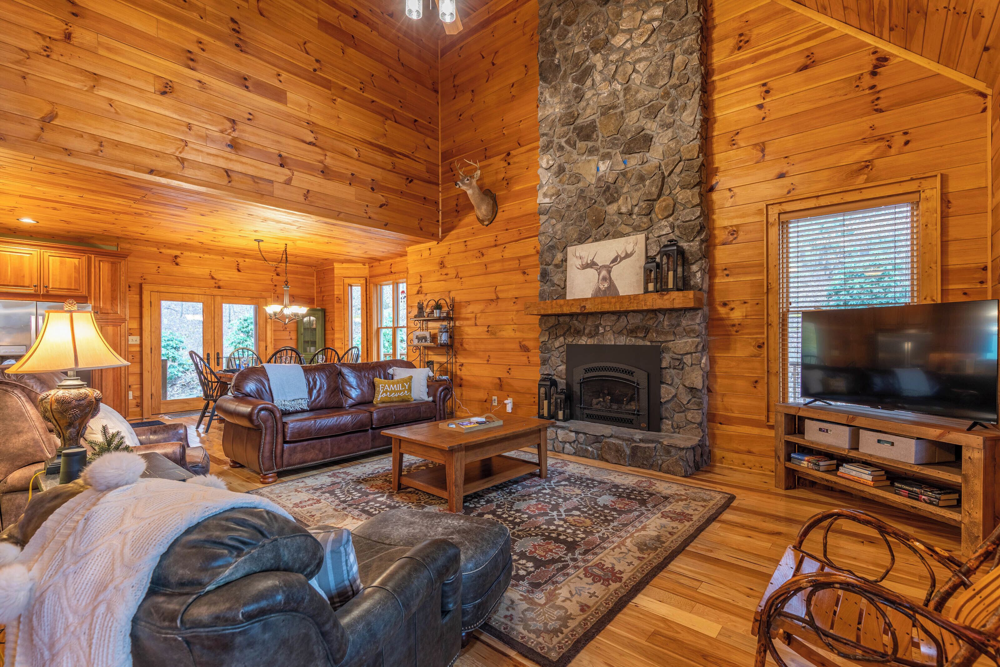 A cozy log cabin interior with a stone fireplace, leather furniture, and a television.