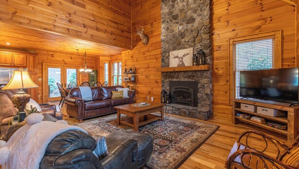 A cozy log cabin interior with a stone fireplace, leather furniture, and a television. - The Forge (Lansing)