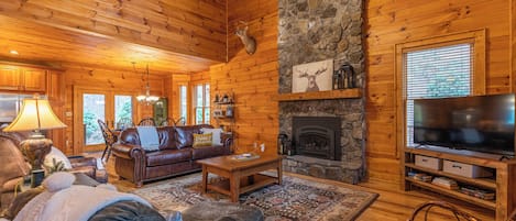 Ein gemütliches Blockhaus-Interieur mit Kamin aus Stein, Ledermöbeln und einem Fernseher.