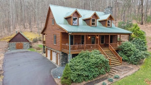 A log cabin with a porch, a stone garage, and a stone chimney. - The Forge (Lansing)