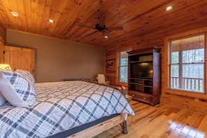 A wooden cabin bedroom with a bed, a ceiling fan, a built-in TV, and a window with blinds. - The Forge (Lansing)