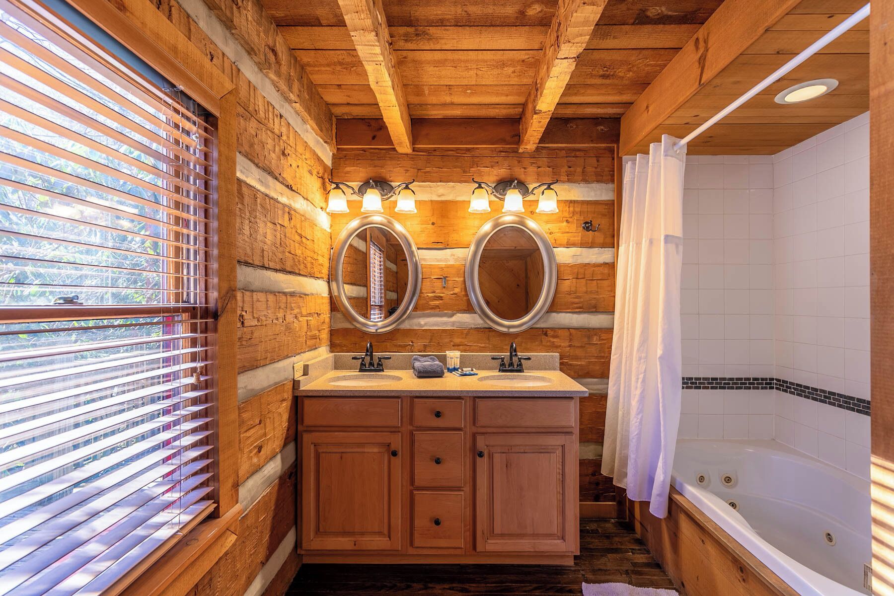 A wooden cabin bathroom with two sinks, a large mirror, and a bathtub.