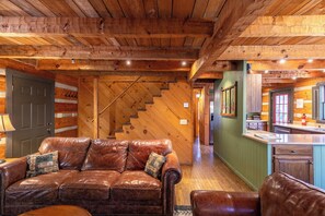 A cozy cabin interior with a leather sofa, wooden staircase, and a kitchen area. - A River Runs Through It (Vilas)