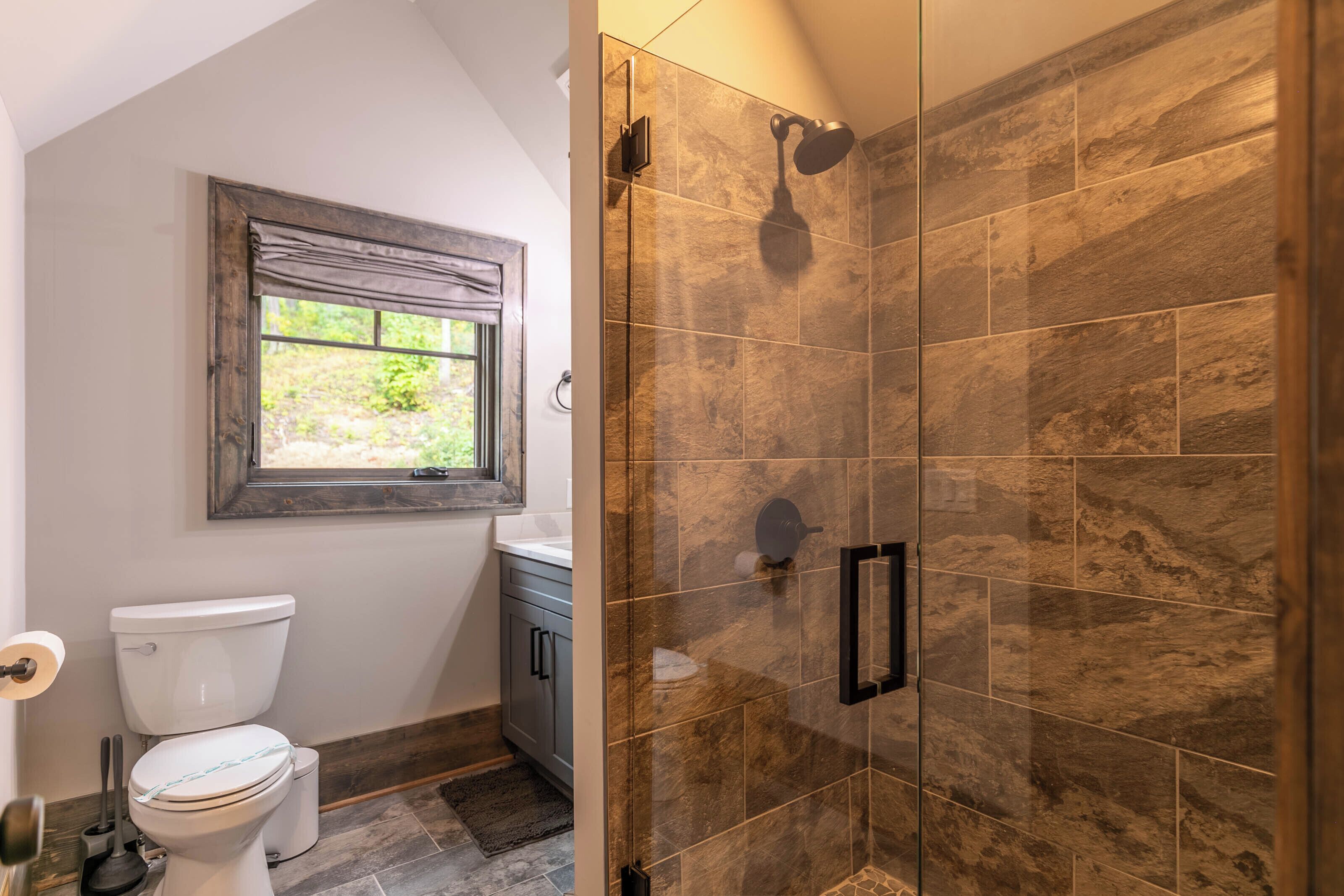 Un baño con inodoro, ventana, ducha con puerta de vidrio y lavamanos.
