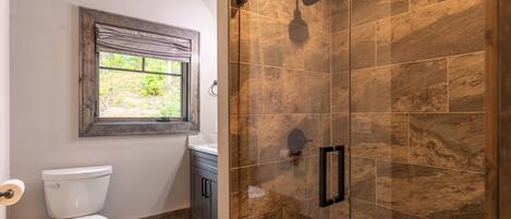 Un baño con inodoro, ventana, ducha con puerta de vidrio y lavamanos.