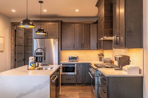 A modern kitchen with stainless steel appliances, a marble countertop, and dark wooden cabinets. - The Cub House at Eagles Nest (Banner Elk)