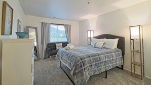 A bedroom with a bed, bedside lamps, a dresser, a chair, and a window with curtains. - 7035 Park City #3R (Park City)