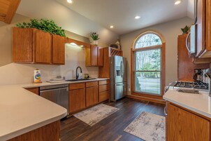 A modern kitchen with wooden cabinets, stainless steel appliances, and a large window with blinds.
