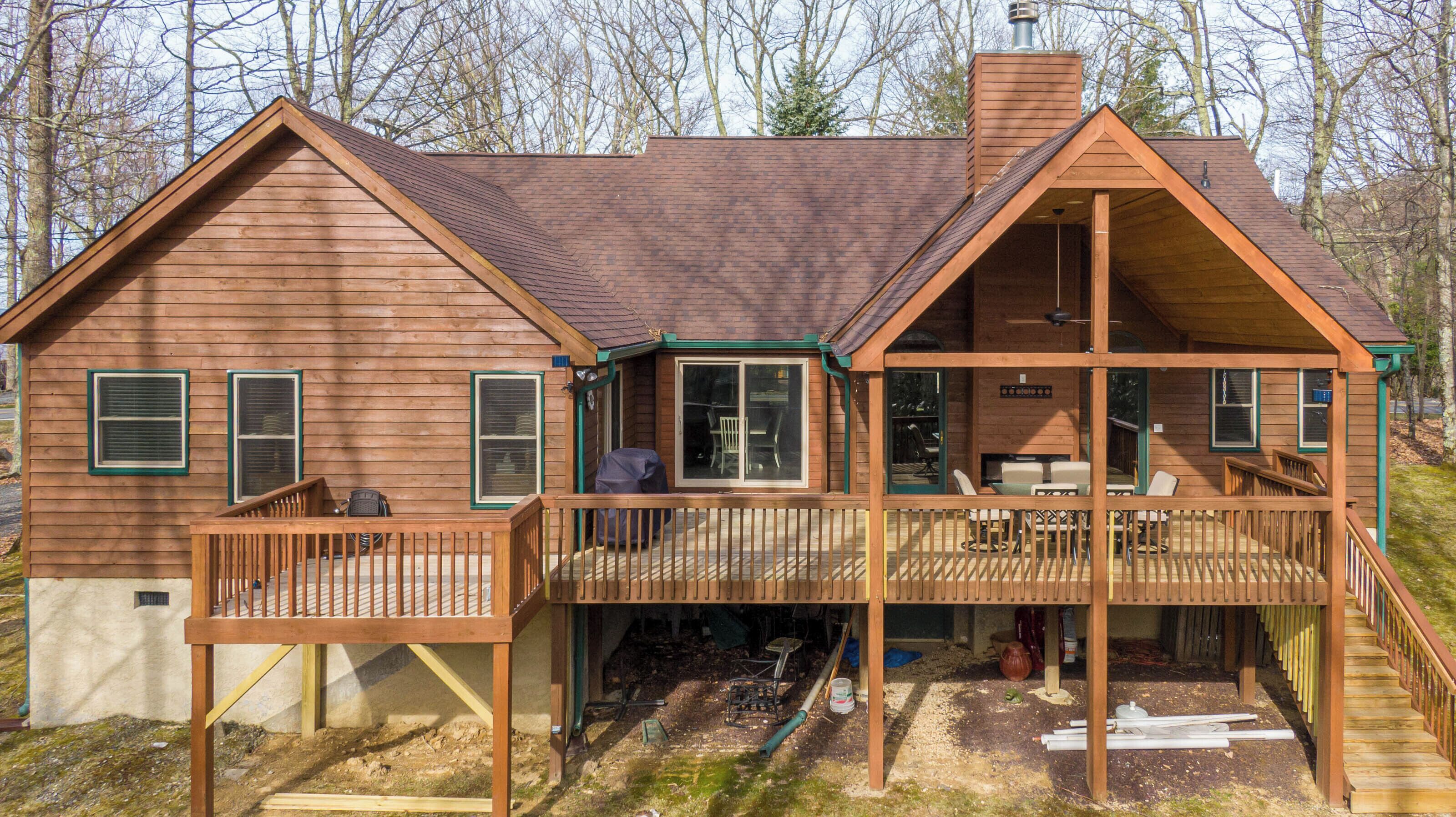 A wooden cabin with a deck, a covered porch, and a chimney.