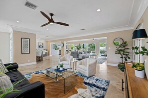 A spacious living room with a ceiling fan, a glass coffee table, a sofa, and a dining area in the background. - Beach Bunny (Fort Lauderdale)