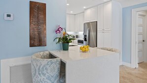 A modern kitchen with white cabinets, a stainless steel refrigerator, and a small island with a plant and lemons. - Beach Bunny (Fort Lauderdale)