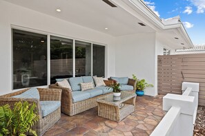 Eine Terrasse im Freien mit Korbmöbeln, einem Glastisch und Topfpflanzen.