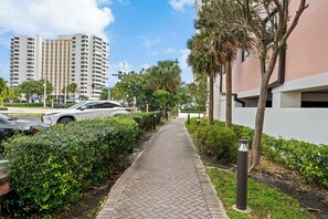 A paved walkway flanked by greenery and modern buildings.