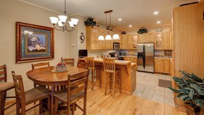 A modern kitchen with wooden cabinets, a stainless steel refrigerator, and a dining area with a wooden table and chairs. - Hebron Falls Cabin (Boone)