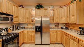 A kitchen with wooden cabinets, a stainless steel refrigerator, a microwave, a stove, and a coffee maker.