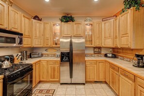 A kitchen with wooden cabinets, a stainless steel refrigerator, a microwave, a stove, and a coffee maker. - Hebron Falls Cabin (Boone)