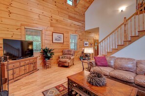 A cozy wooden interior with a TV, leather sofa, and a staircase. - Hebron Falls Cabin (Boone)